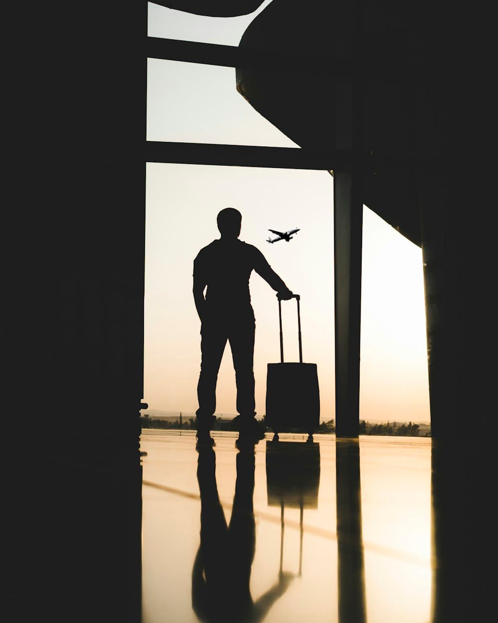 Traveller silhouetted at an airport window with a suitcase